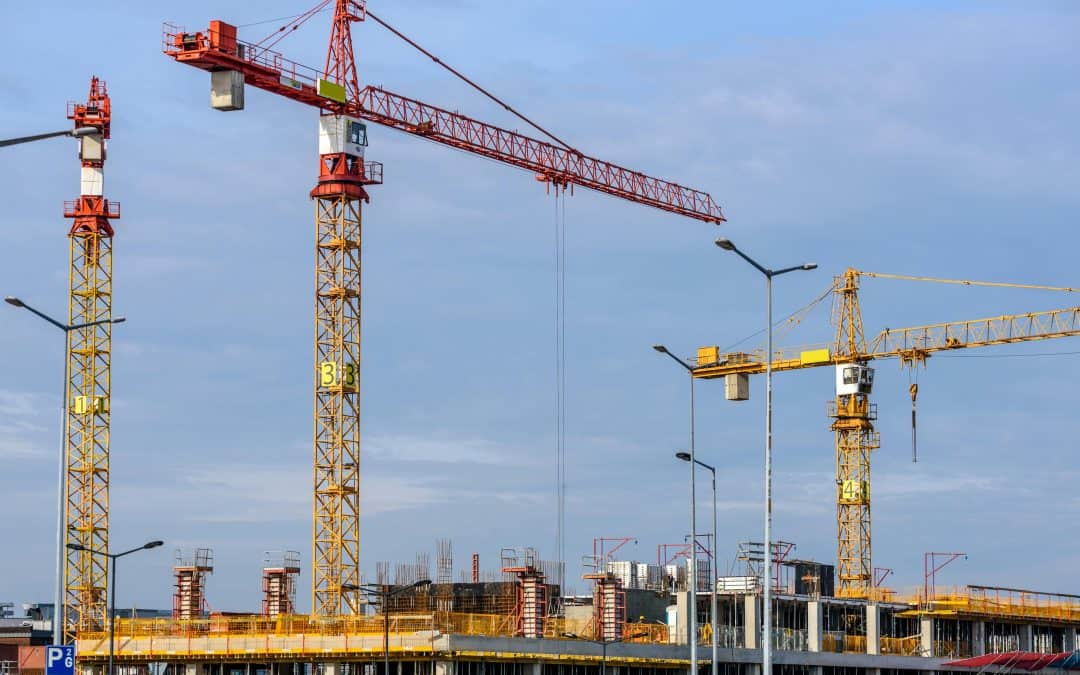 Three yellow and red tower cranes under clear blue sky