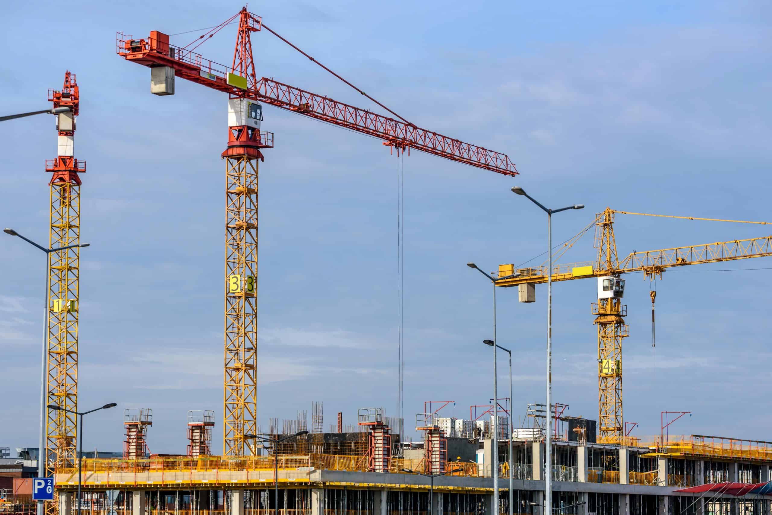 Three yellow and red tower cranes under clear blue sky