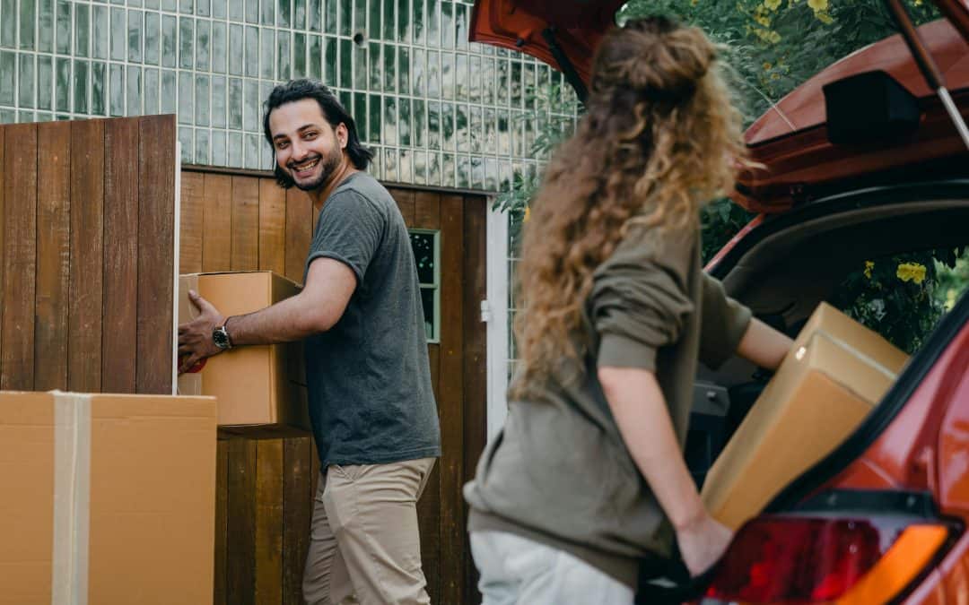 Happy couple unloading automobile while moving apartment in summer day